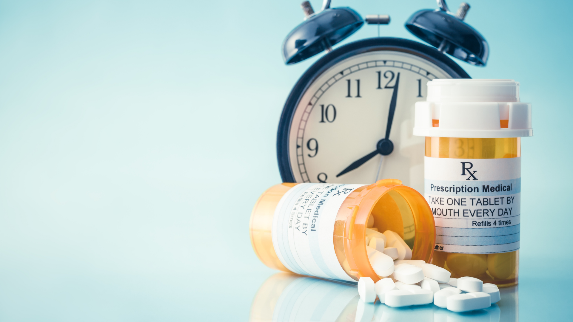 Prescription medicine bottles and tablets beside an alarm clock.