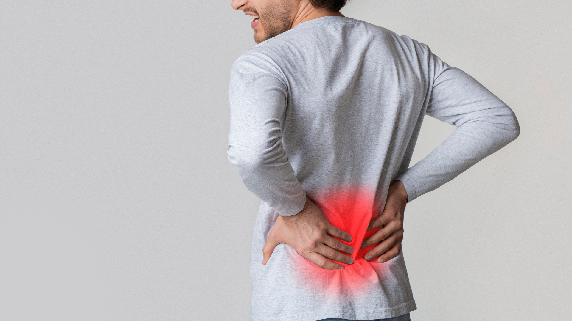 A man in a grey long-sleeved shirt holding his lower back, with a red glowing area indicating pain.