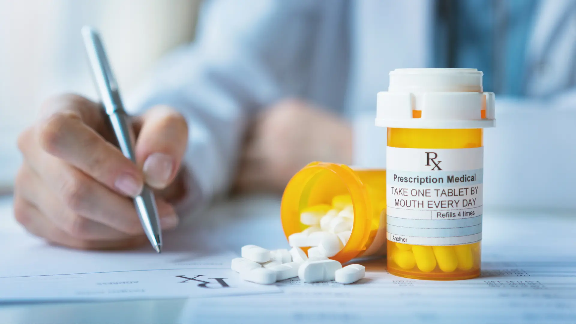 A prescription pill bottle beside a hand writing on a prescription form.