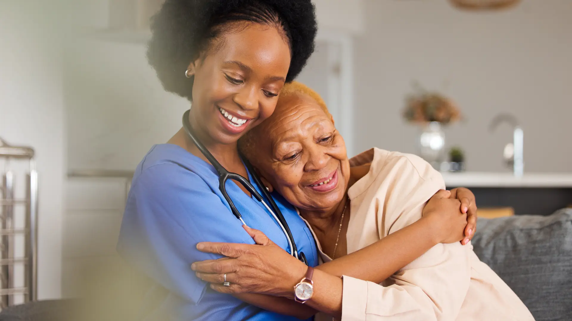 A Troy Medicare nurse in blue scrubs warmly embraces a smiling older adult member at home.